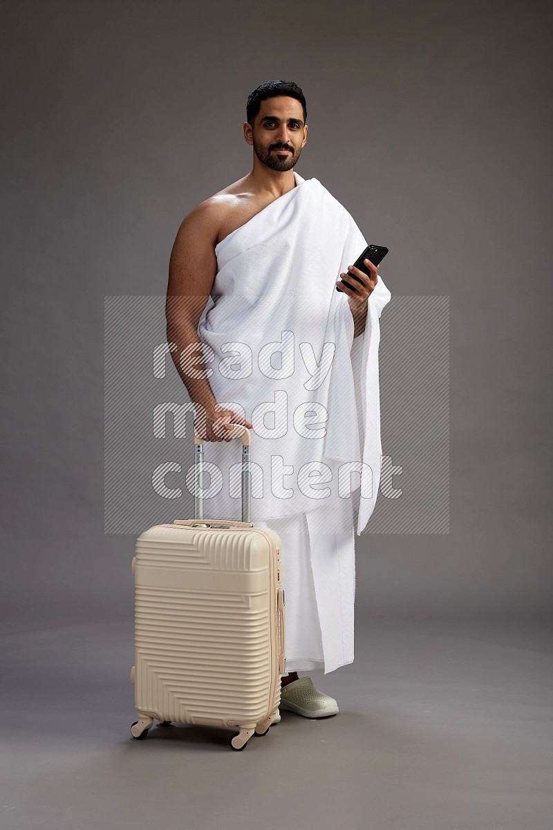 A man wearing Ehram Standing holding traveling bag on gray background