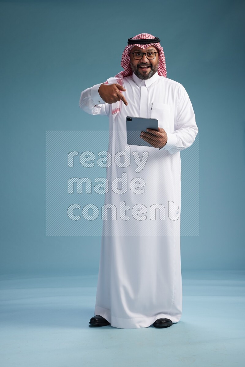 Saudi Man with shimag Standing holding a tablet on blue background