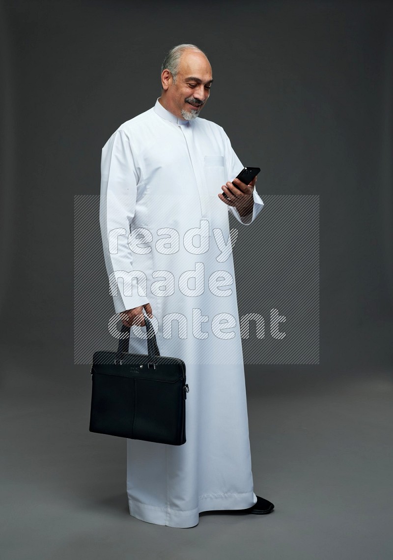 Saudi man without shomag Standing holding bag and phone on gray background