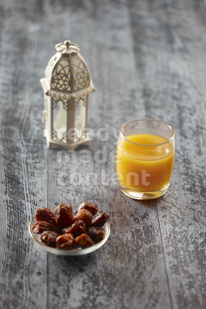 A white lantern with different drinks, dates, nuts, prayer beads and quran on grey wooden background