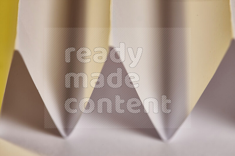 A close-up abstract image showing sharp geometric paper folds in white gradients and warm tones