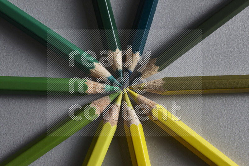 An arrangement of colored pencils in shades of green and yellow on grey background