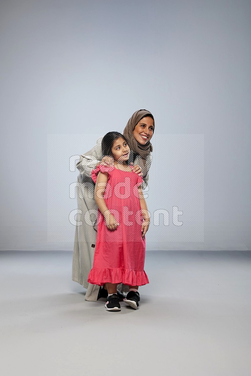 A girl and her mother interacting with the camera on gray background