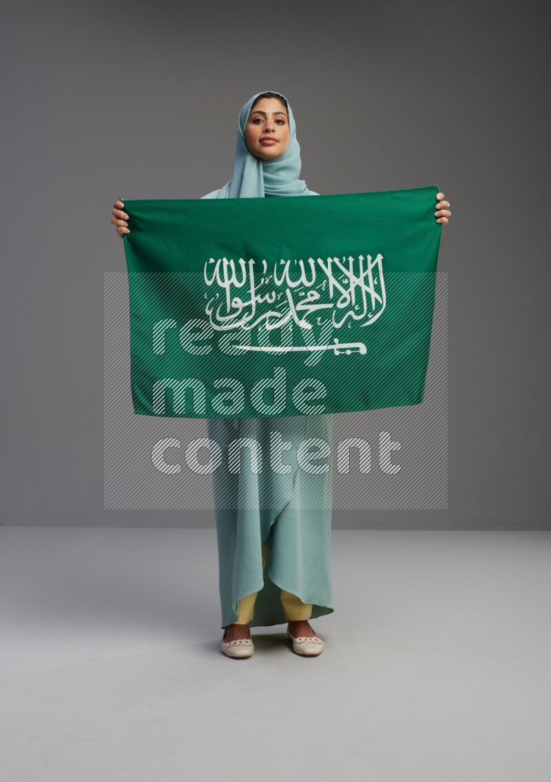 Saudi Woman wearing Abaya standing holding Saudi flag on Gray background