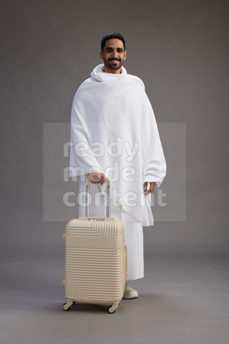 A man wearing Ehram Standing holding traveling bag on gray background