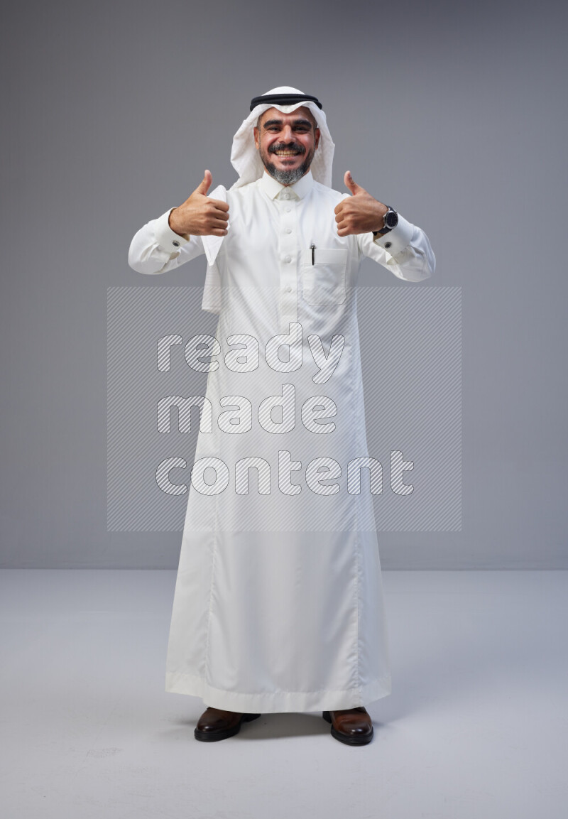 Saudi man Wearing Thob and white Shomag standing interacting with the camera on Gray background