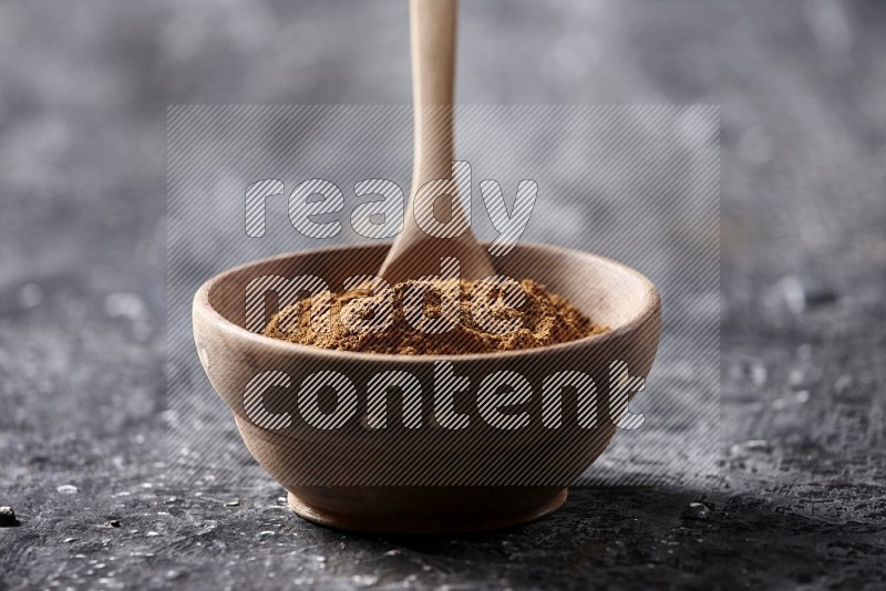 Wooden bowl full of cinnamon powder with a wooden spoon on a textured black background in different angles