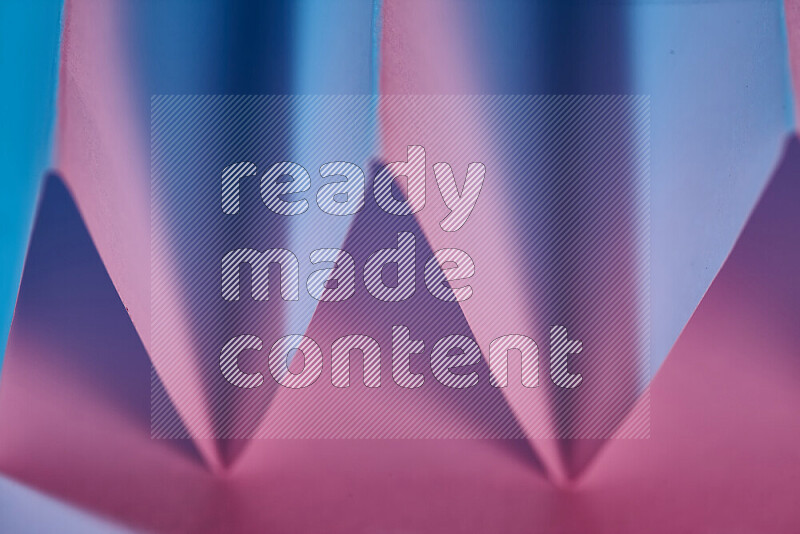 A close-up abstract image showing sharp geometric paper folds in blue and pink gradients