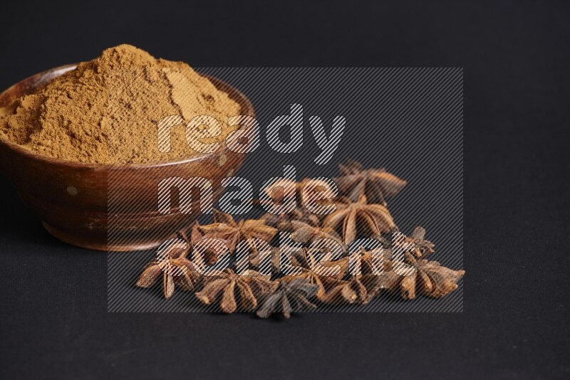Star Anise powder in a wooden bowl with star anise beside it on a black background