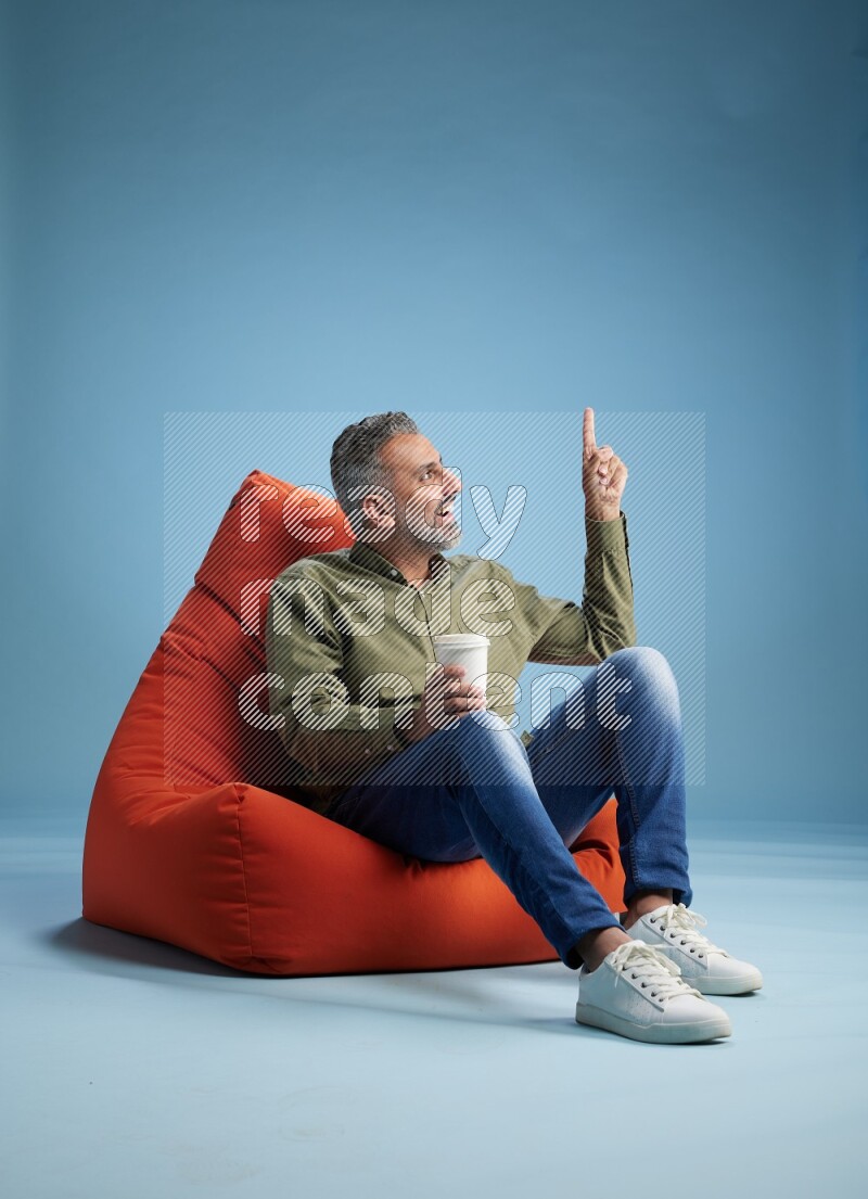 A man sitting on an orange beanbag and drinking coffee