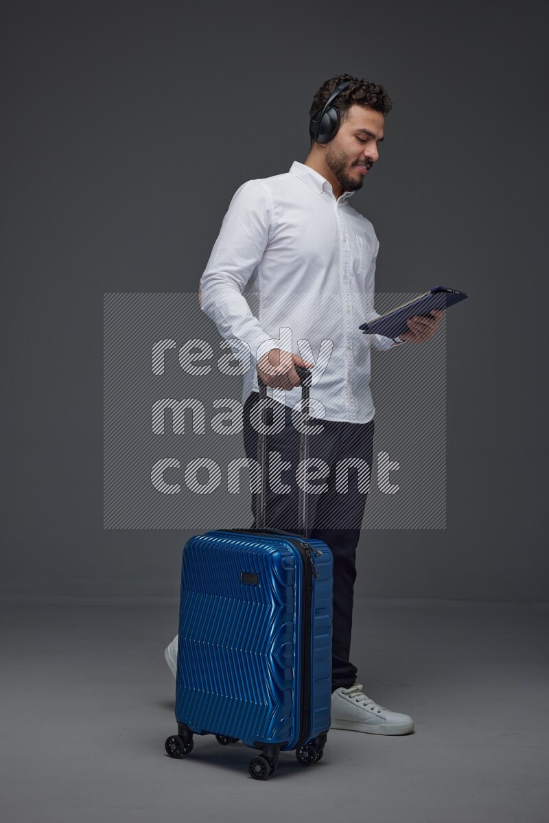 A man wearing smart casual with and pulling a carry-on luggage eye level on a gray background