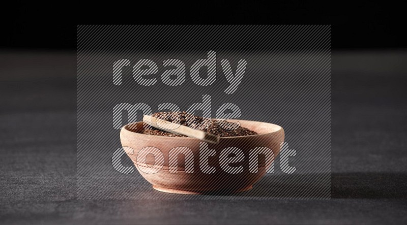 وعاء خشبي ممتلئ بحبوب بذر الكتان مع ملعقة خشبية ممتلئة بالحبوب علي خلفية سوداء