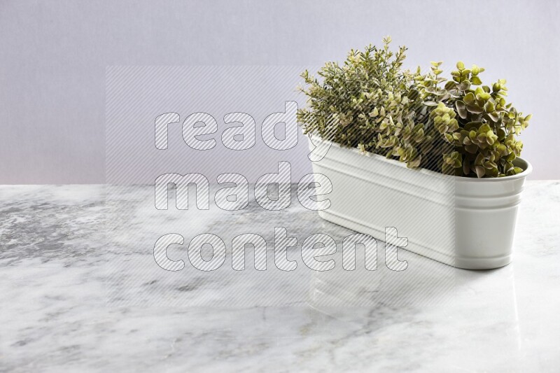 Multiple green artificial plants in white pot on grey marble background