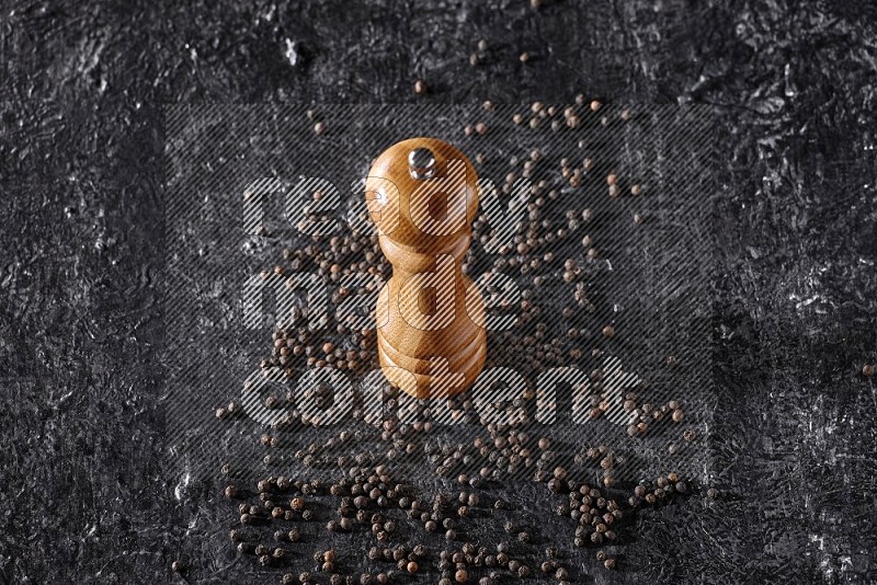 A wooden grinder with black pepper beads on a textured black flooring