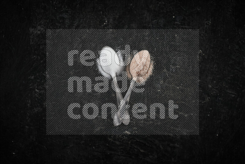 ملعقتان معدنيتان ممتلئتان بالملح الأبيض وملح الهيمالايا الوردي على خلفية سوداء