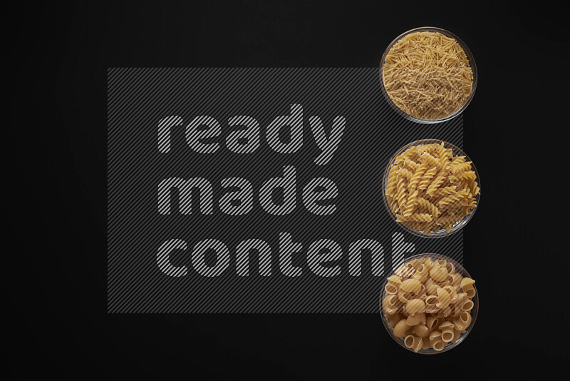 Different pasta types in 3 glass bowls on black background