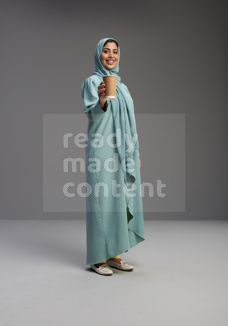 Saudi Woman wearing Abaya standing  holding paper cup on Gray background