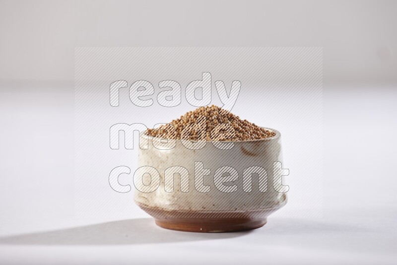 A beige pottery bowl full of mustard seeds on white flooring