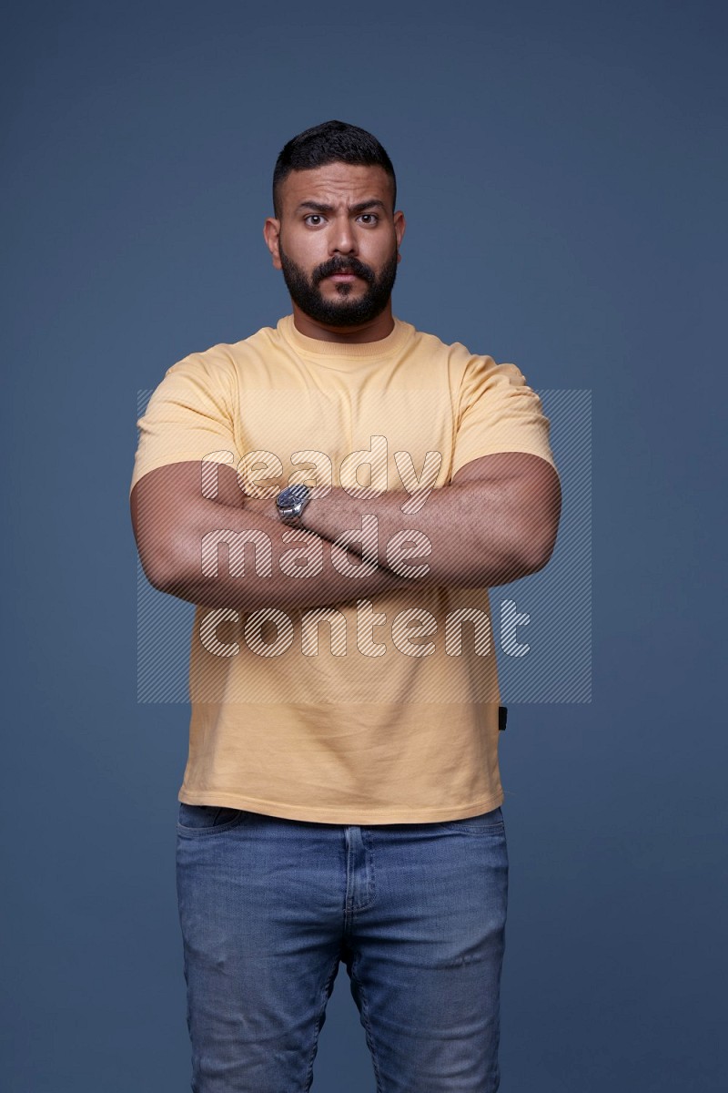 A man posing in a blue background wearing a yellow shirt