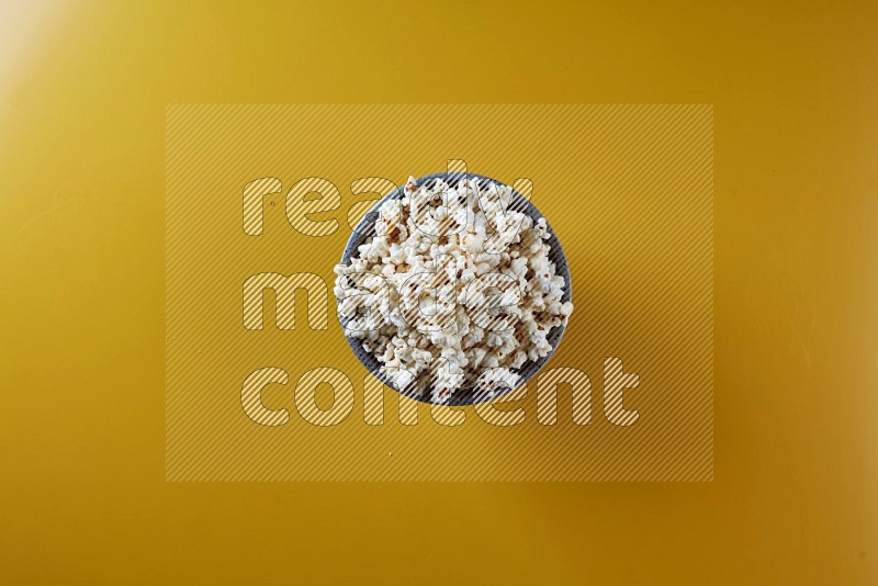 A multicolored pottery bowl full of popcorn on a yellow background in different angles