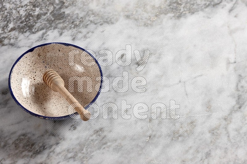 Multicolored Pottery bowl with wooden honey handle in it, on grey marble flooring, 65 degree angle