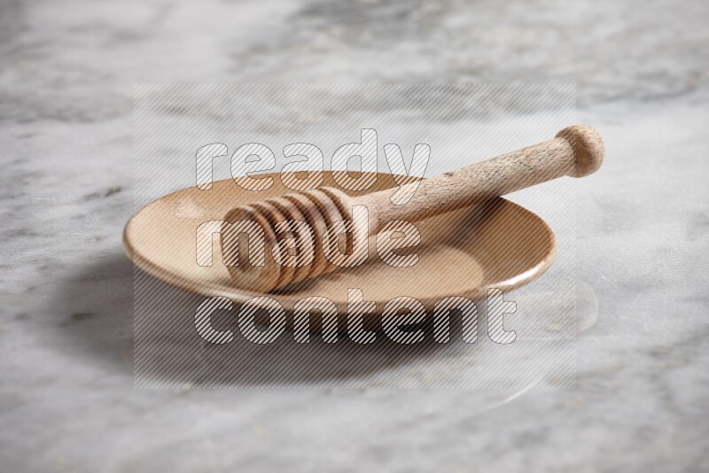 Beige pottery plate with wooden honey dipper in it on grey marble background