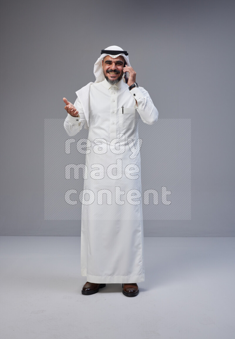 Saudi man Wearing Thob and white Shomag standing talking on phone on Gray background