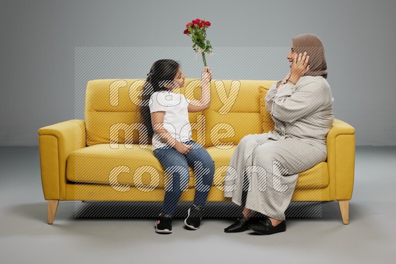 A girl sitting giving flowers to her mother on gray background