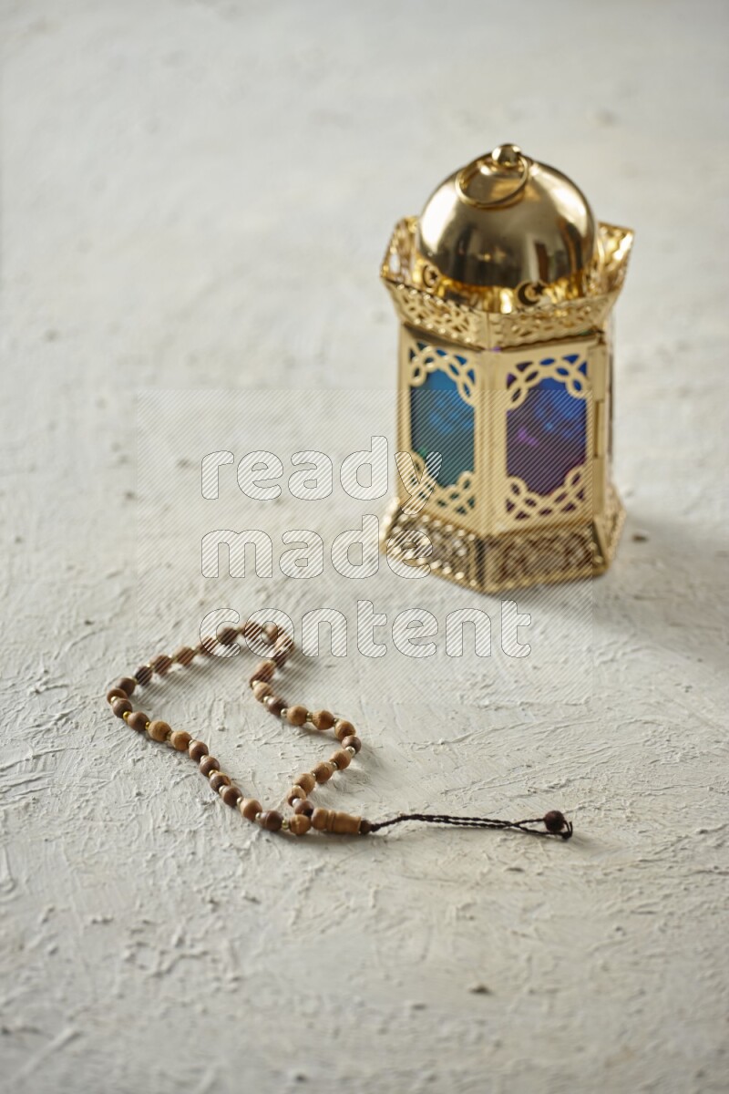 A golden lantern with different drinks, dates, nuts, prayer beads and quran on textured white background