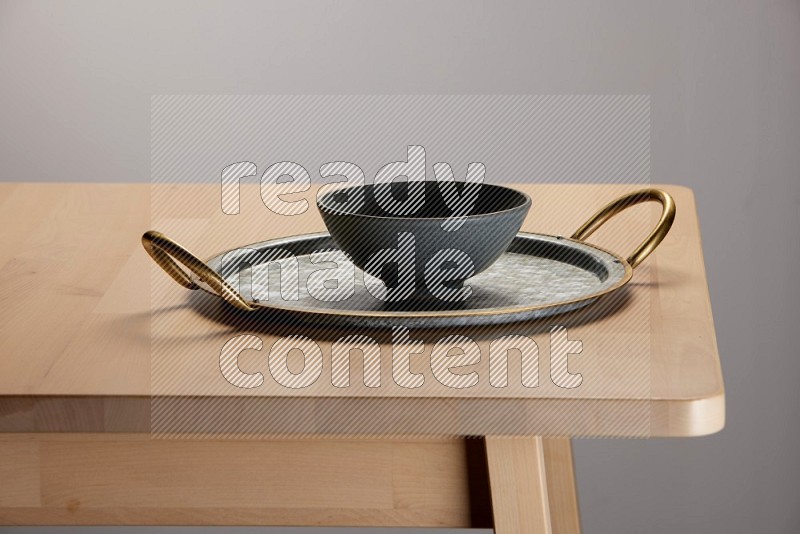 grey bowl placed on a rounded stainless steel tray with golden handels on the edge of wooden table