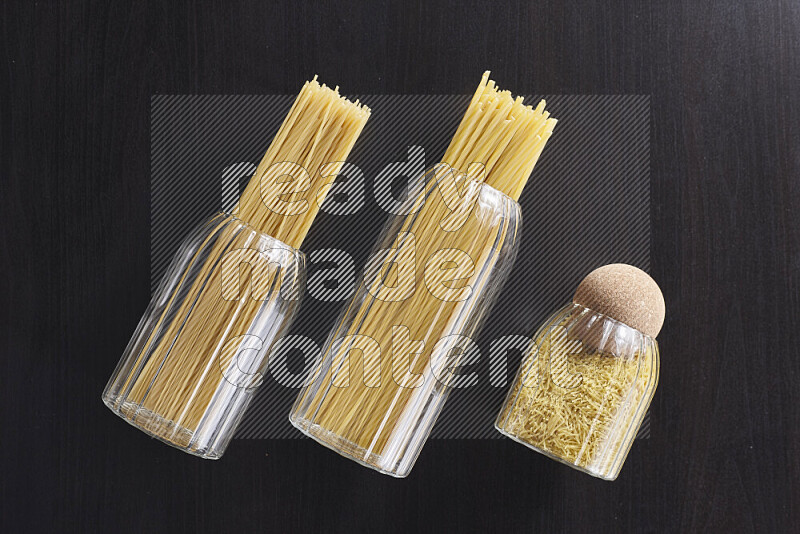 Raw pasta in glass jars on black background