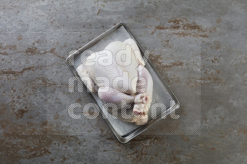 whole Raw chicken on a small oven trey direct on a rustic grey background