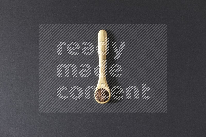 A wooden spoon full of cloves powder on a black flooring