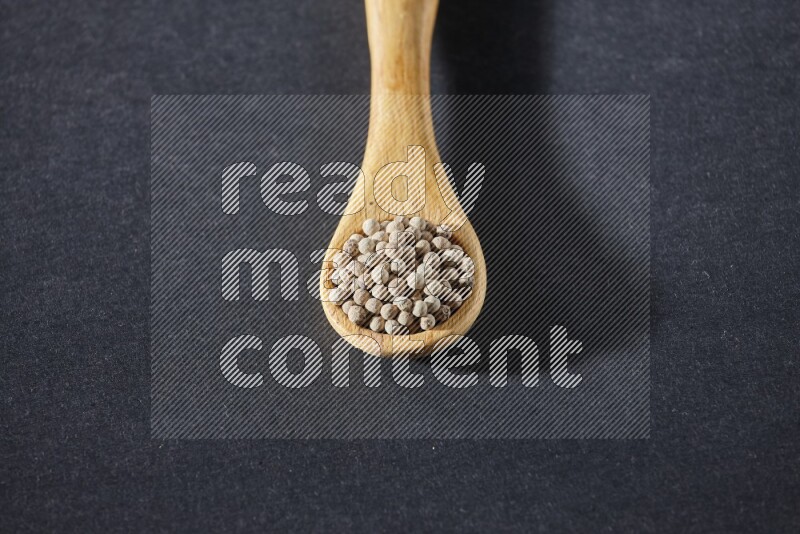A wooden spoon full of white pepper beads on black flooring