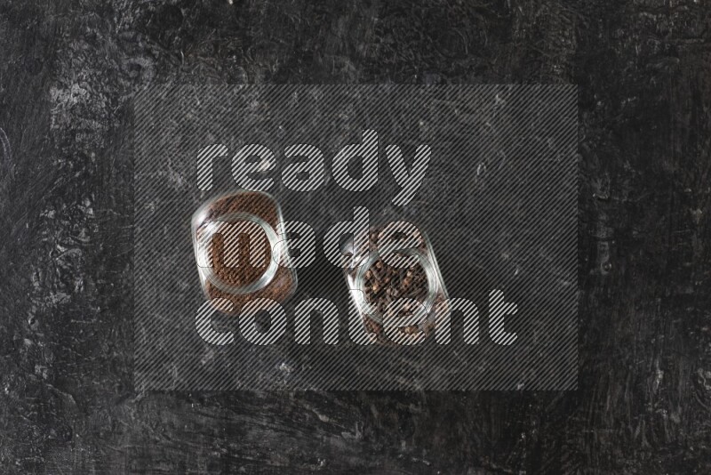 وعاءان زجاجيان ممتلئان بالقرنفل وبودرة القرنفل على أرضية سوداء