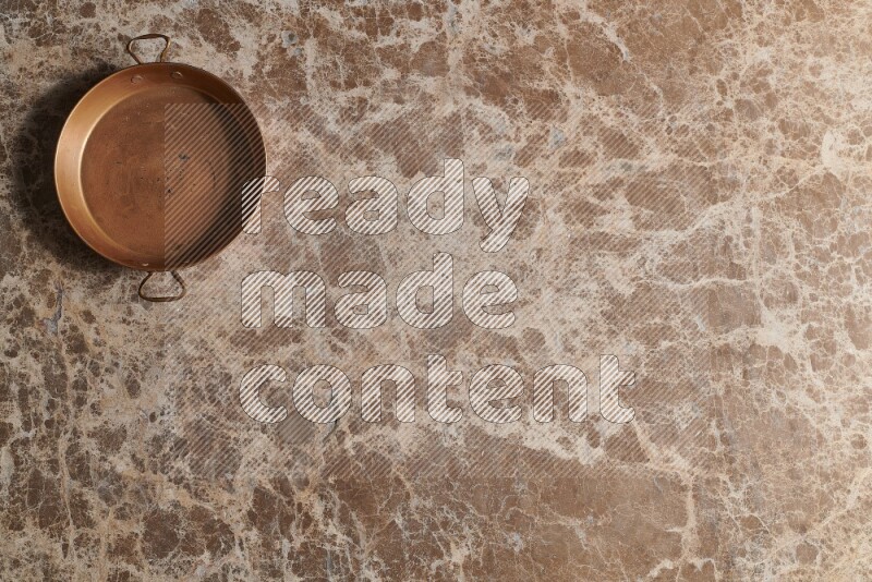 A small copper pan on beige marble background