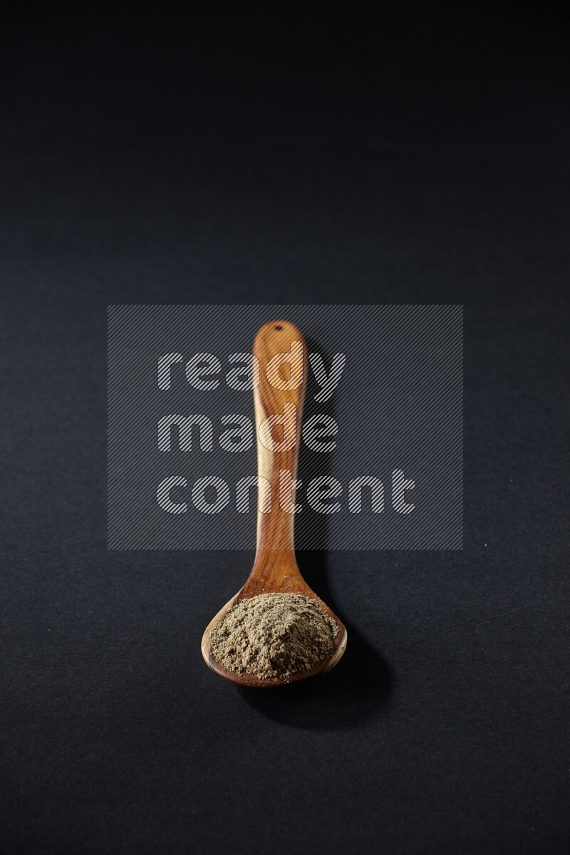 A wooden ladle full of cardamom powder on black flooring