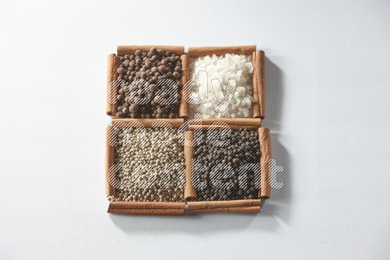 4 مربعات من أعواد القرفة ممتلئة ببهار الفلفل الحلو والملح الأبيض والفلفل الأبيض والفلفل الأسود على أرضية بيضاء