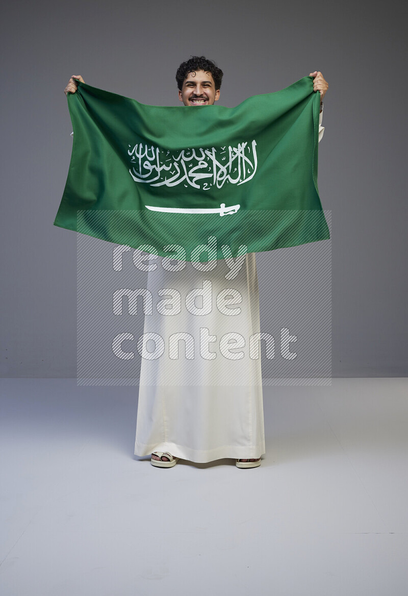 رجل سعودي يرتدي ثوب ويحمل علم السعودية
