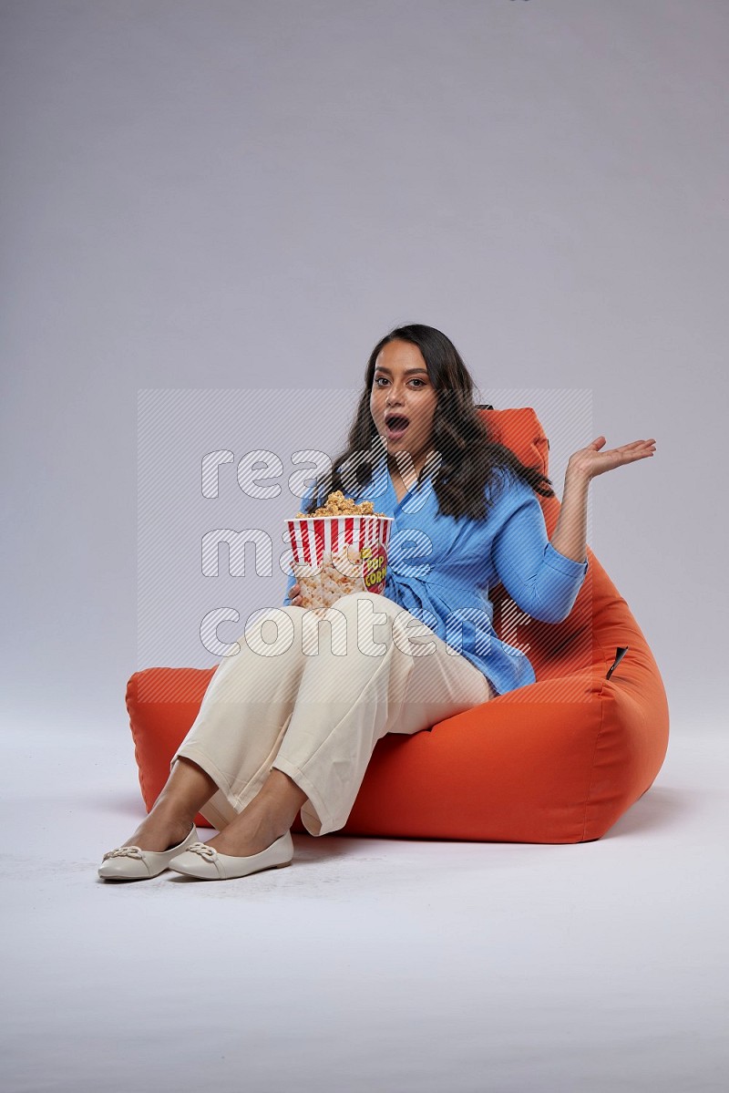 A woman sitting on an orange beanbag and eating popcorn