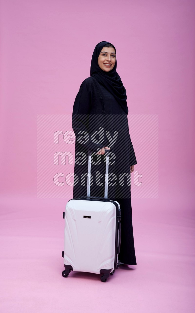 Saudi woman wearing Abaya standing holding bag on pink background