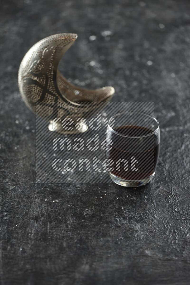 A silver lantern with different drinks, dates, nuts, prayer beads and quran on textured black background
