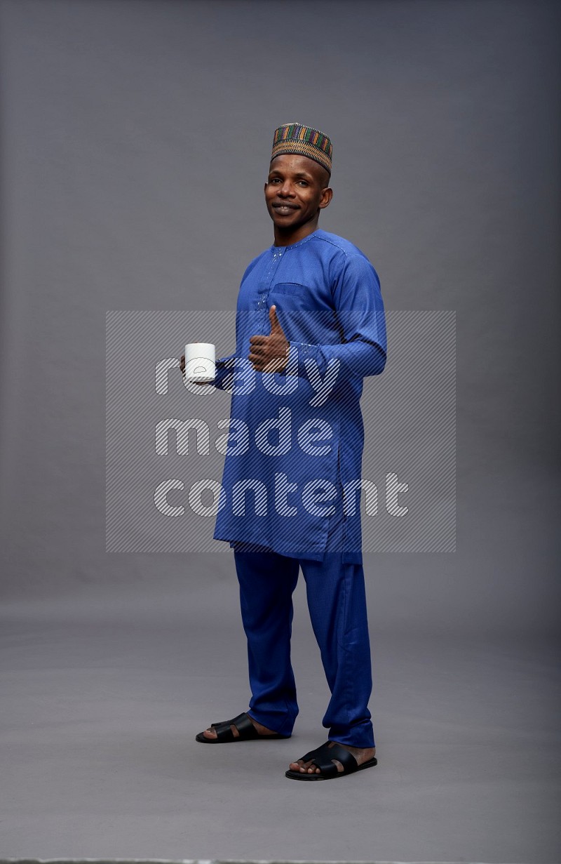 Man wearing Nigerian outfit standing holding mug on gray background