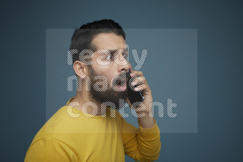 A man having a calling in a blue background wearing a yellow shirt