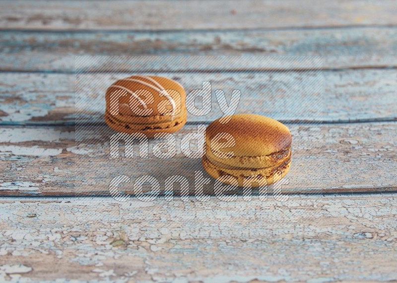 45º Shot of of two assorted Brown Irish Cream, and Yellow Crème Brulée macarons on light blue background