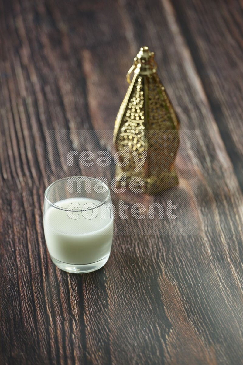 A golden lantern with different drinks, dates, nuts, prayer beads and quran on brown wooden background