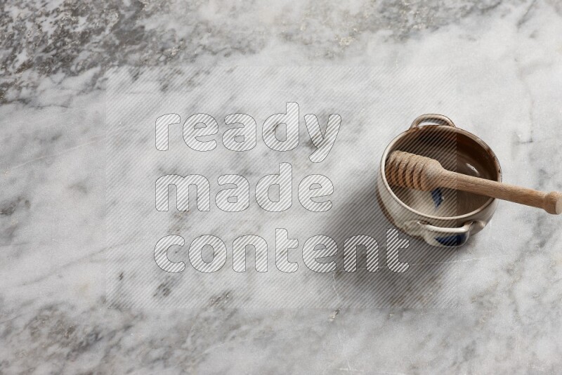 Multicolored pottery bowl with wooden honey dipper in it on grey marble background