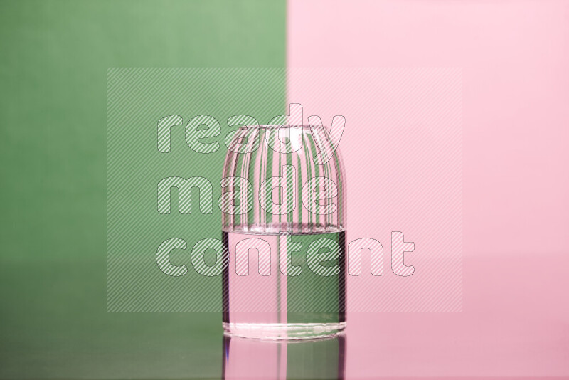 The image features a clear glassware filled with water, set against green and rose background