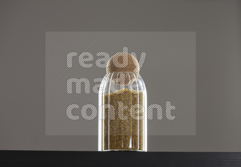 Coarse bulgur in a glass jar on black background