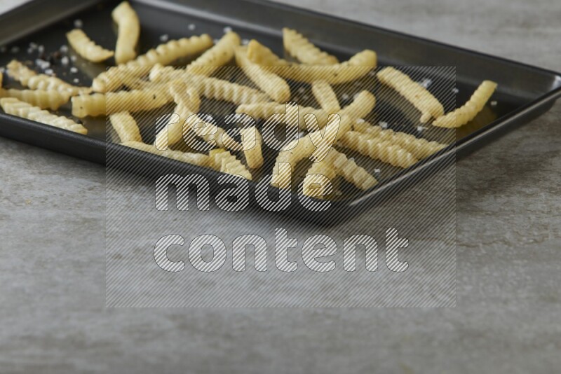 crinkle fries in a black stainless steel rectangle tray on grey textured counter top